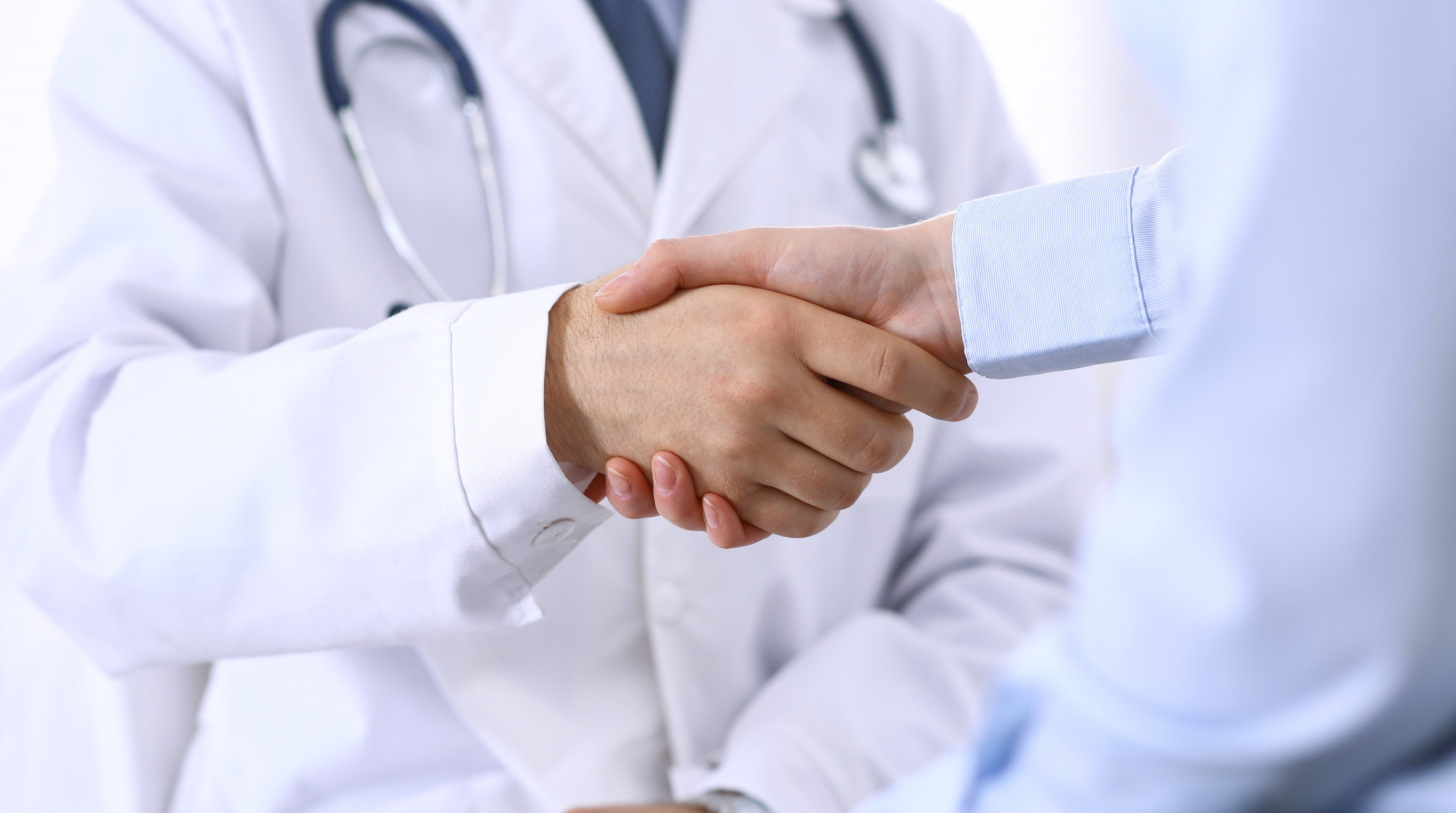Male doctor and woman patient shaking hands. Partnership in medicine, trust and medical ethics concept.