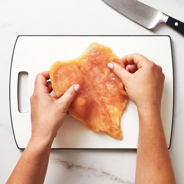 Close up of hands opening a butterflied chicken breast