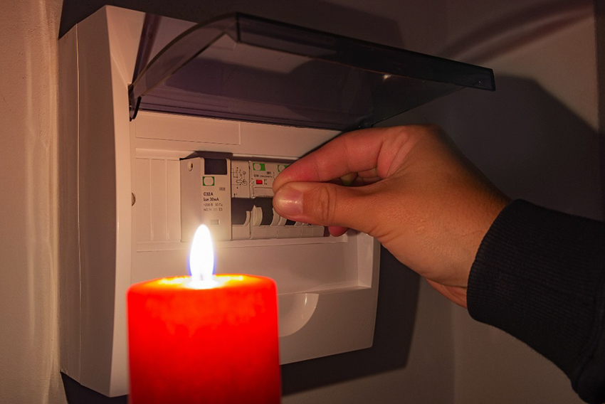Roka na sliki preverja sanje varovalk v električni omarici. Simbolna slika za izpad elektrike in električni mrk