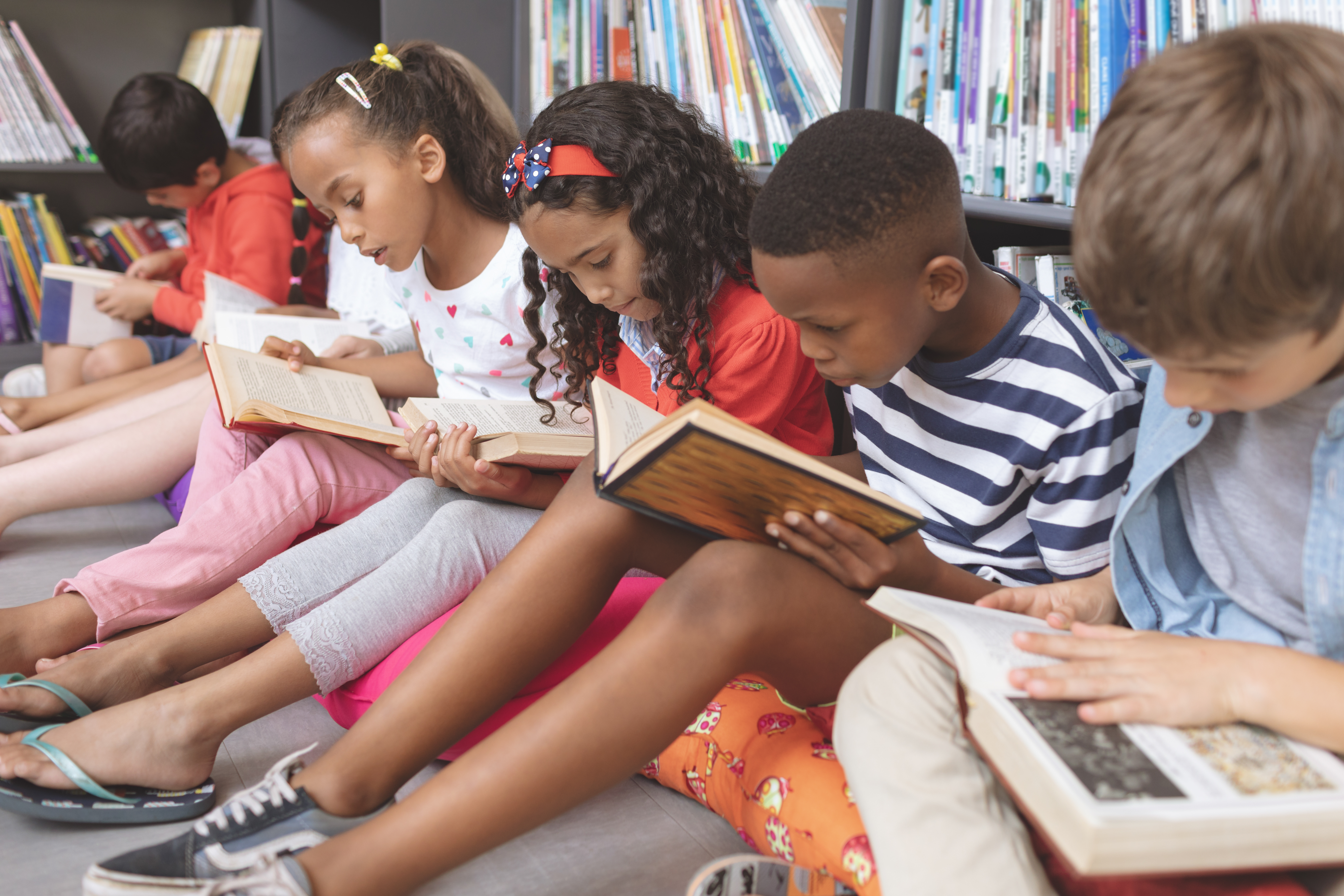 School kids sitting on cushions and studying over books in a library