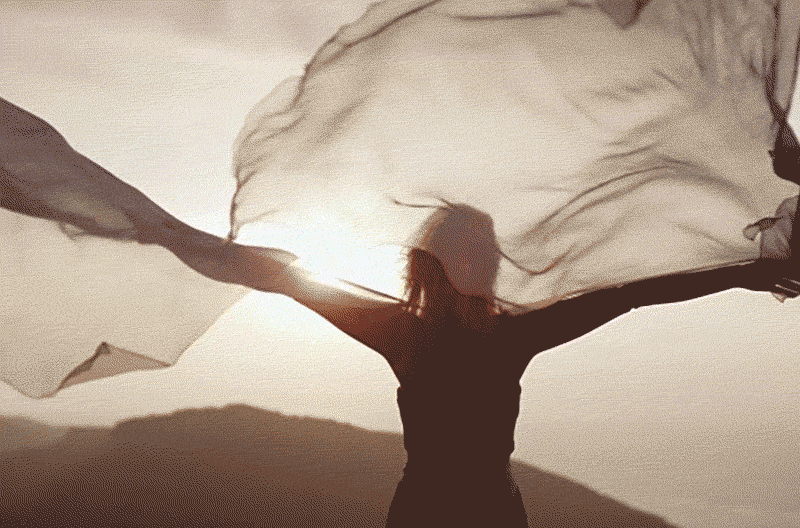 Woman standing cliffside with billowing fabric