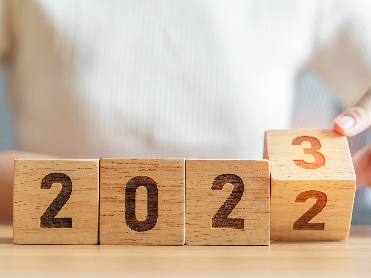 A man in a white T-shirt sitting at a table changes wooden blocks reading 2022 to 2023. 