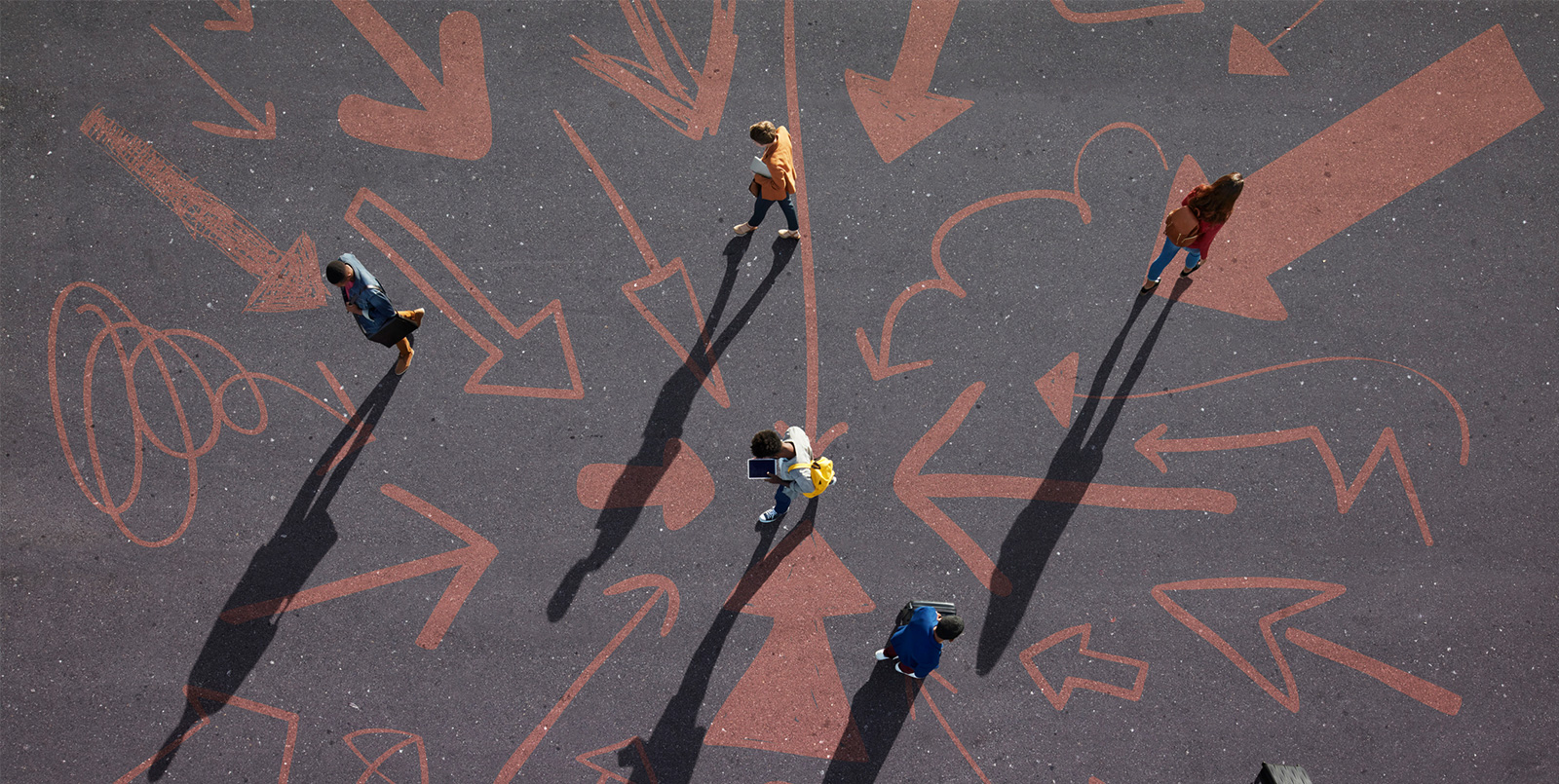 Five people walking around on a blacktop with red chalked arrows drawn on it