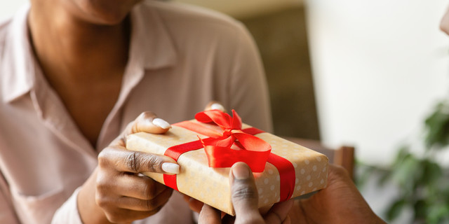 Unrecognizable black guy giving his girlfriend birthday gift at cafe, closeup of hands