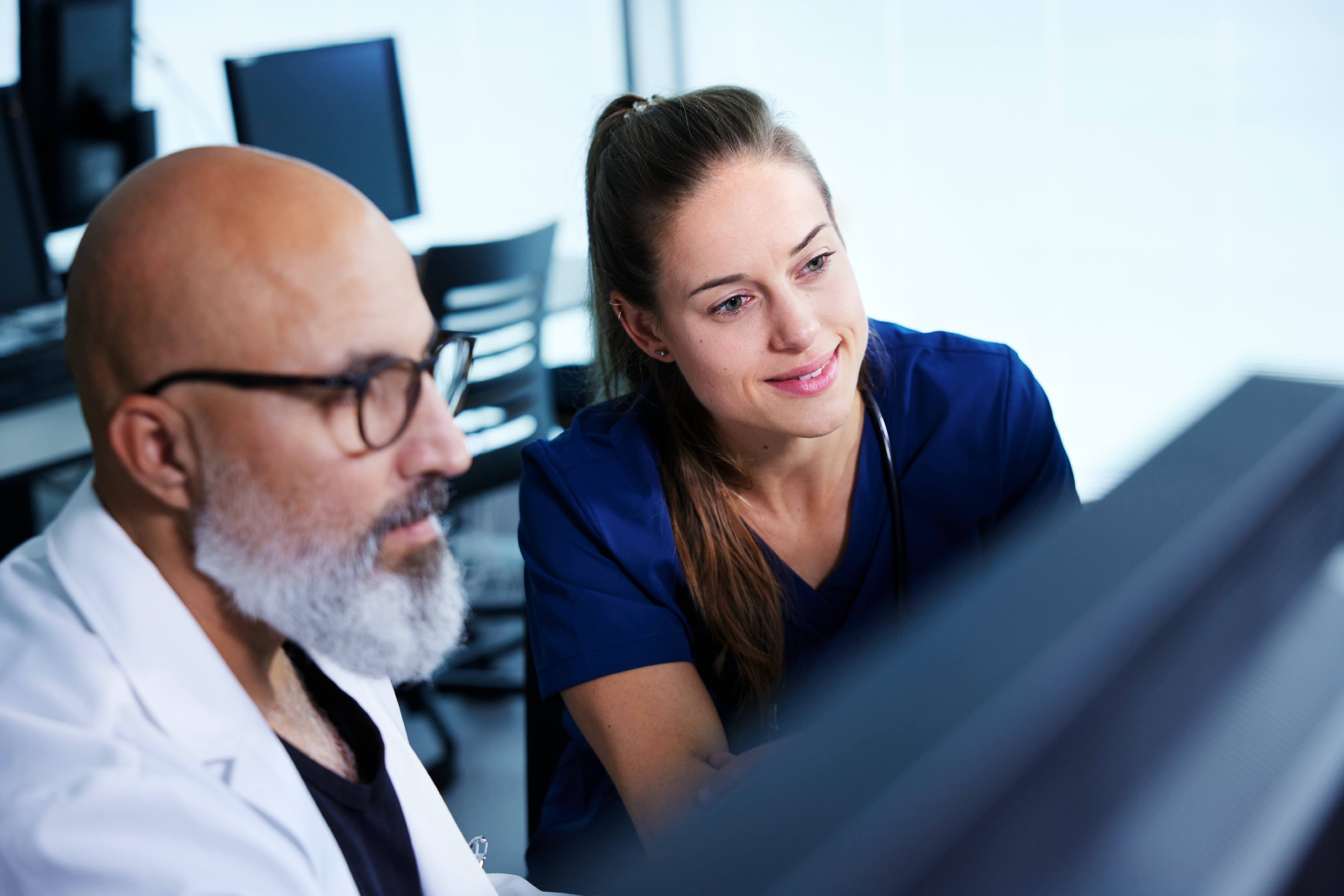A male and female healthcare worker collaborate while looking at a monitor.