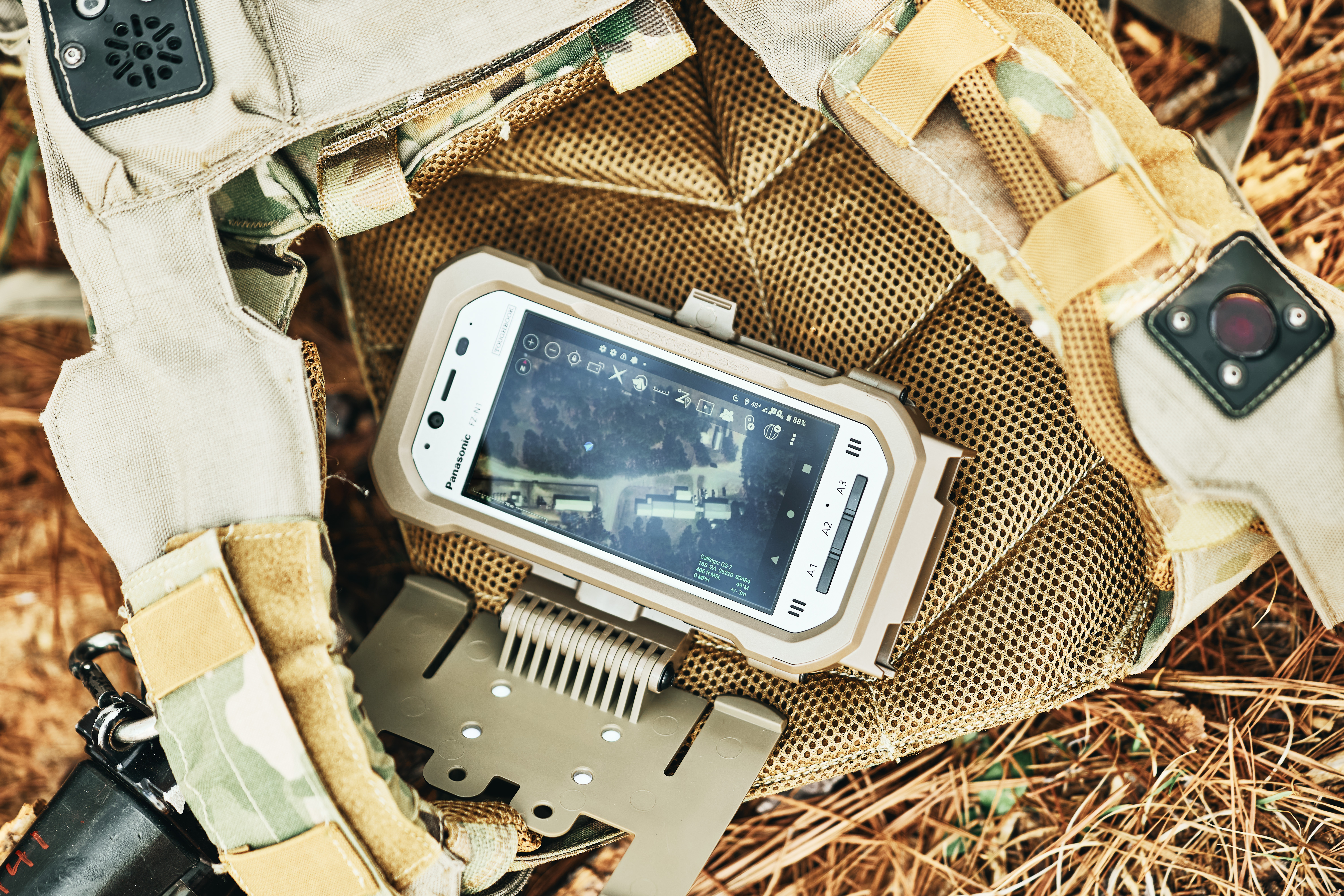 A piece of mobile military technology sitting on a backpack in the field.