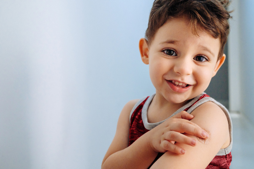 Deček kaže ramo, kamor je bil cepljen - Simbolna fotgrafija za cepljenje otrok in cepiva