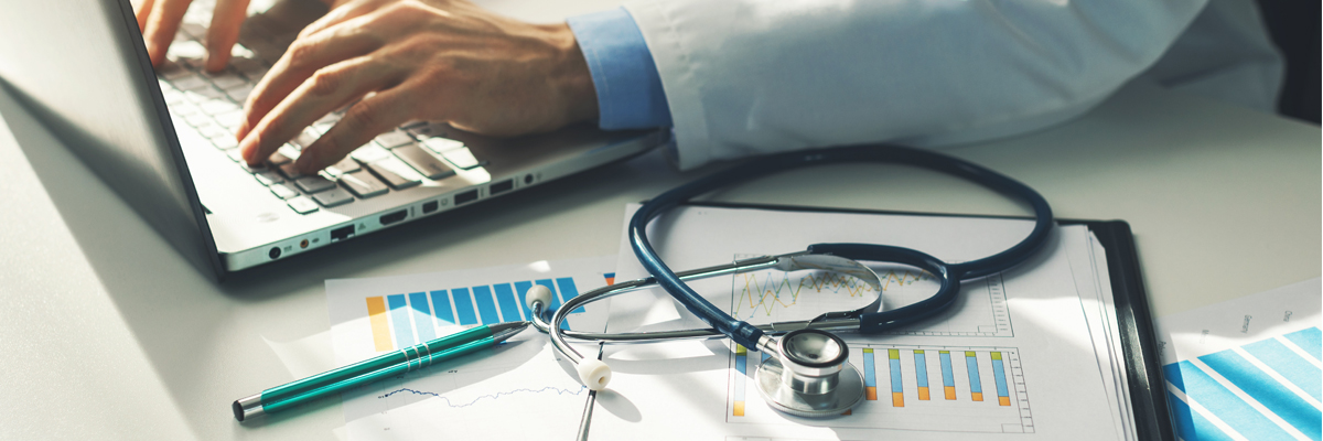 A healthcare provider uses a calculator while working on laptop