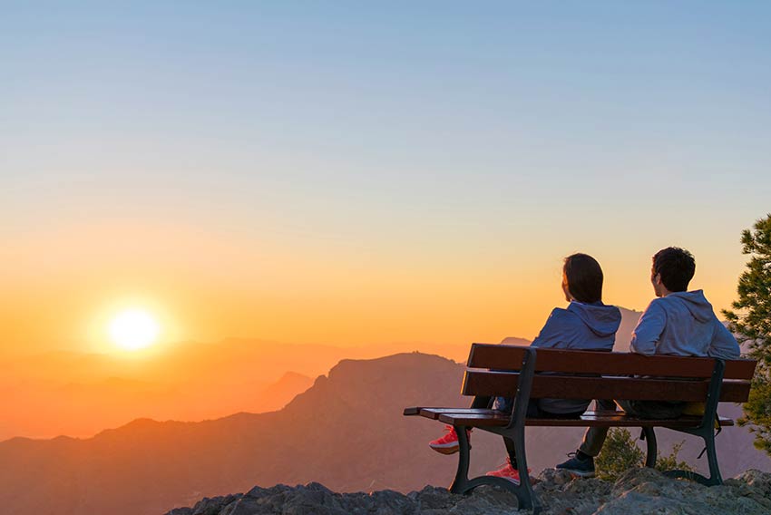 Pokojninsko zavarovanje sklenite, ko ste mladi - mlad par sedi na klopci v hribih in občudije sončni vzhod