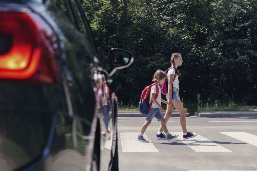 Pešca punca in fant prečkata cesto na zebri, medtem avto stoji pred prehodom