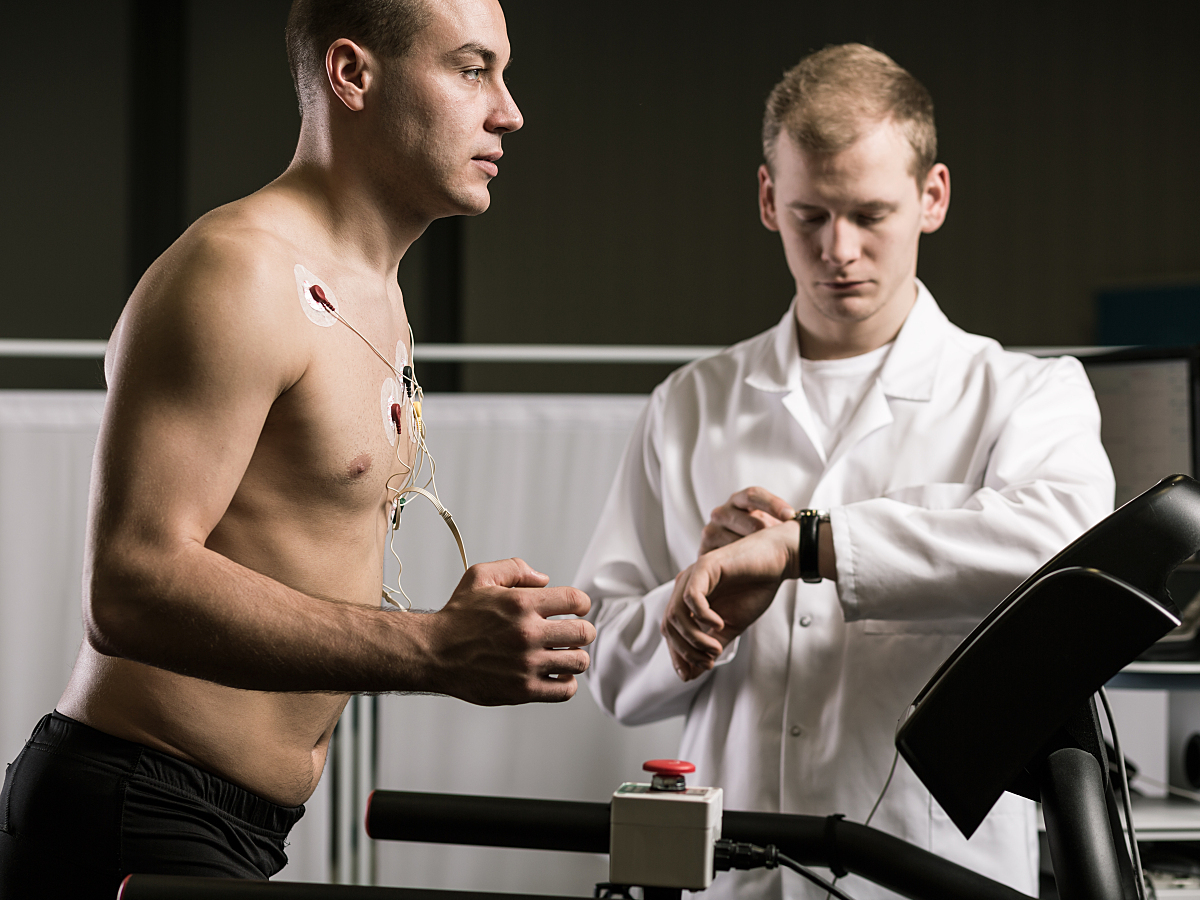 A man performs a treadmill exercise test while a doctor watches and monitors his exercise capacity.