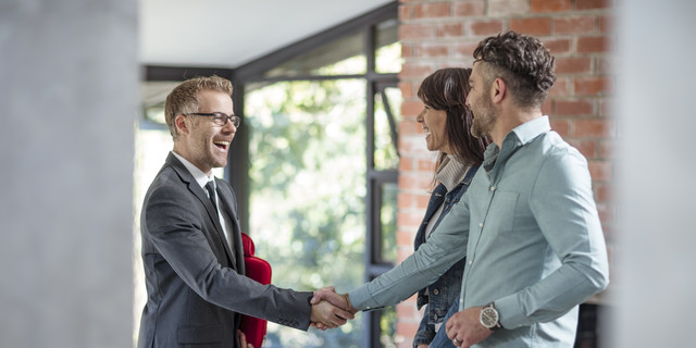 Estate agent shaking hands with couple in empty home