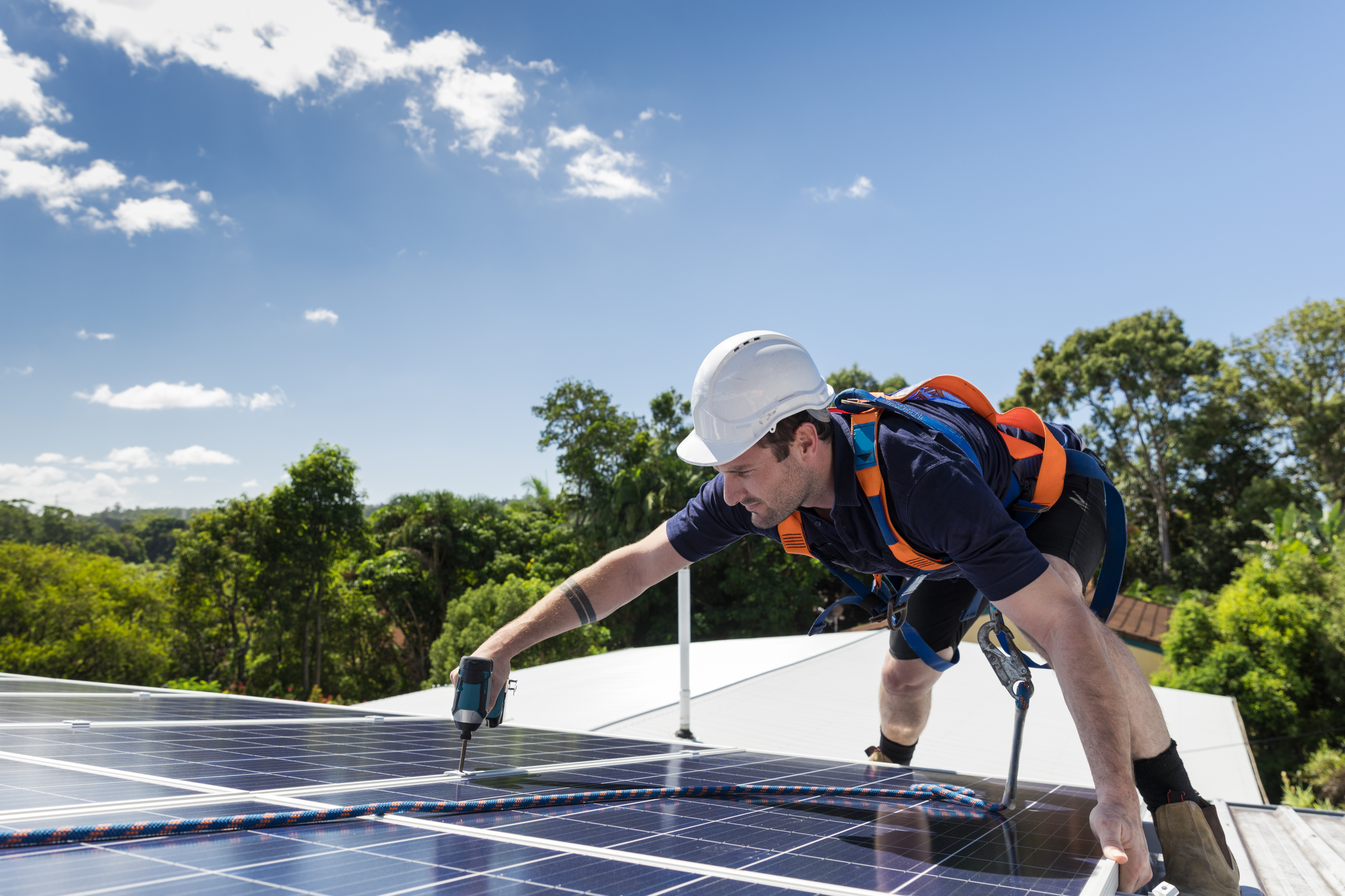 Solar panel technician with drill installing solar panels on roof