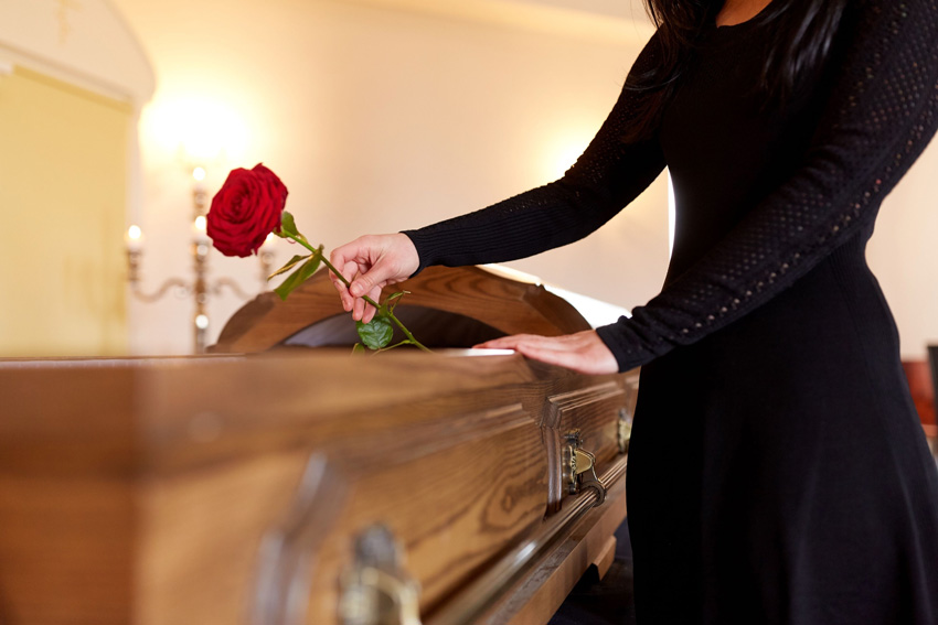 Žalno oblečena ženska odlaga vrtnico na krsto na pogrebu organiziranem za svojca.