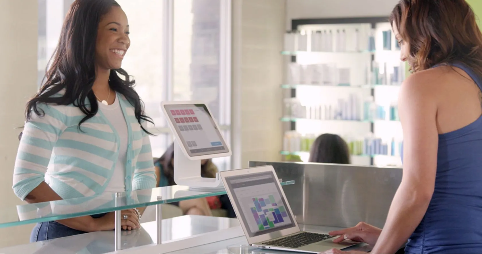 Photo of customer at the counter of a salon, with employee behind the counter using a laptop with Square Appointments interface