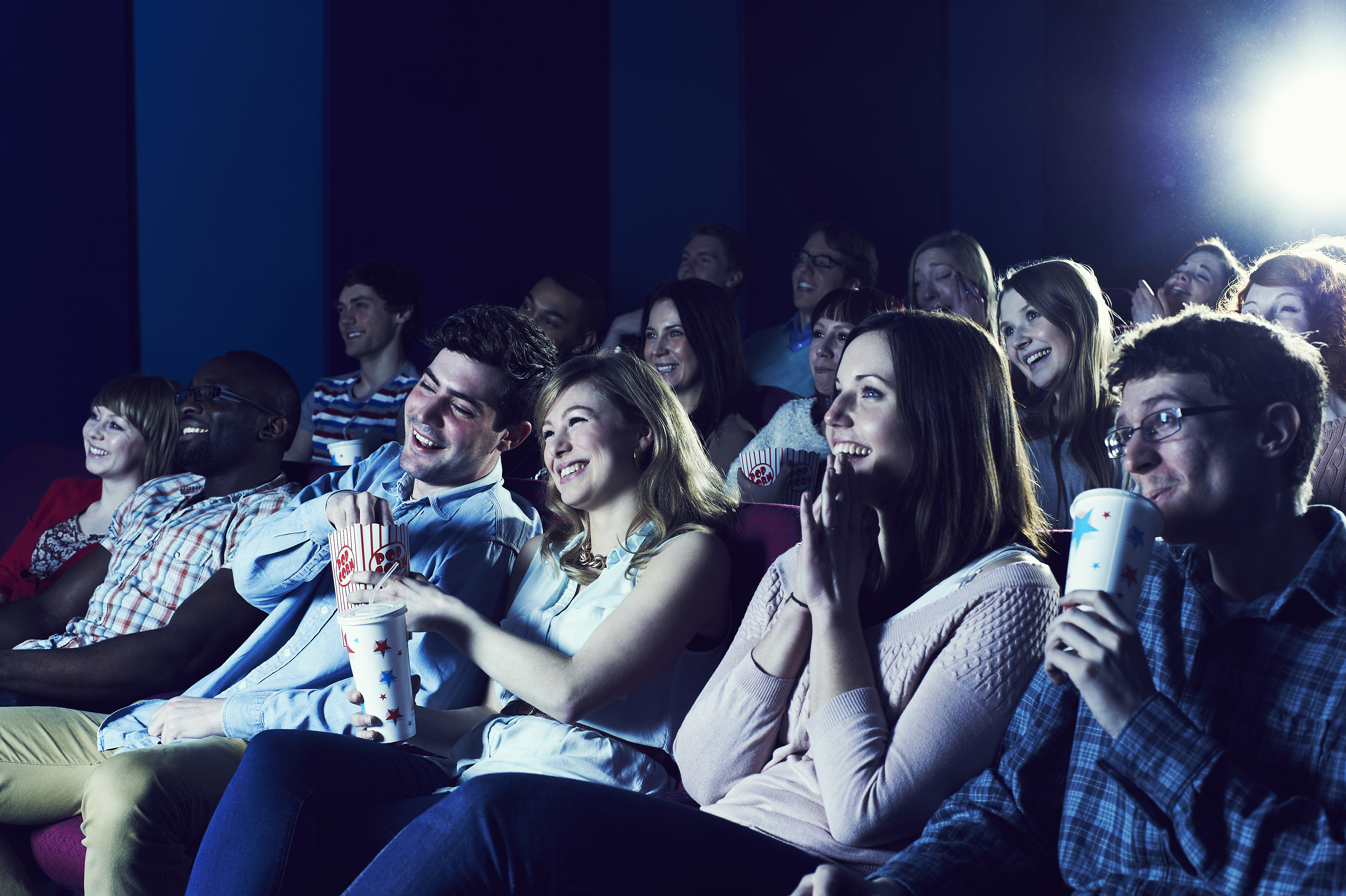 People enjoy a live event in a movie theater while sharing popcorn.