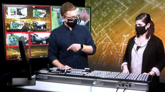 Two professionals on a live broadcast in front of a soundboard