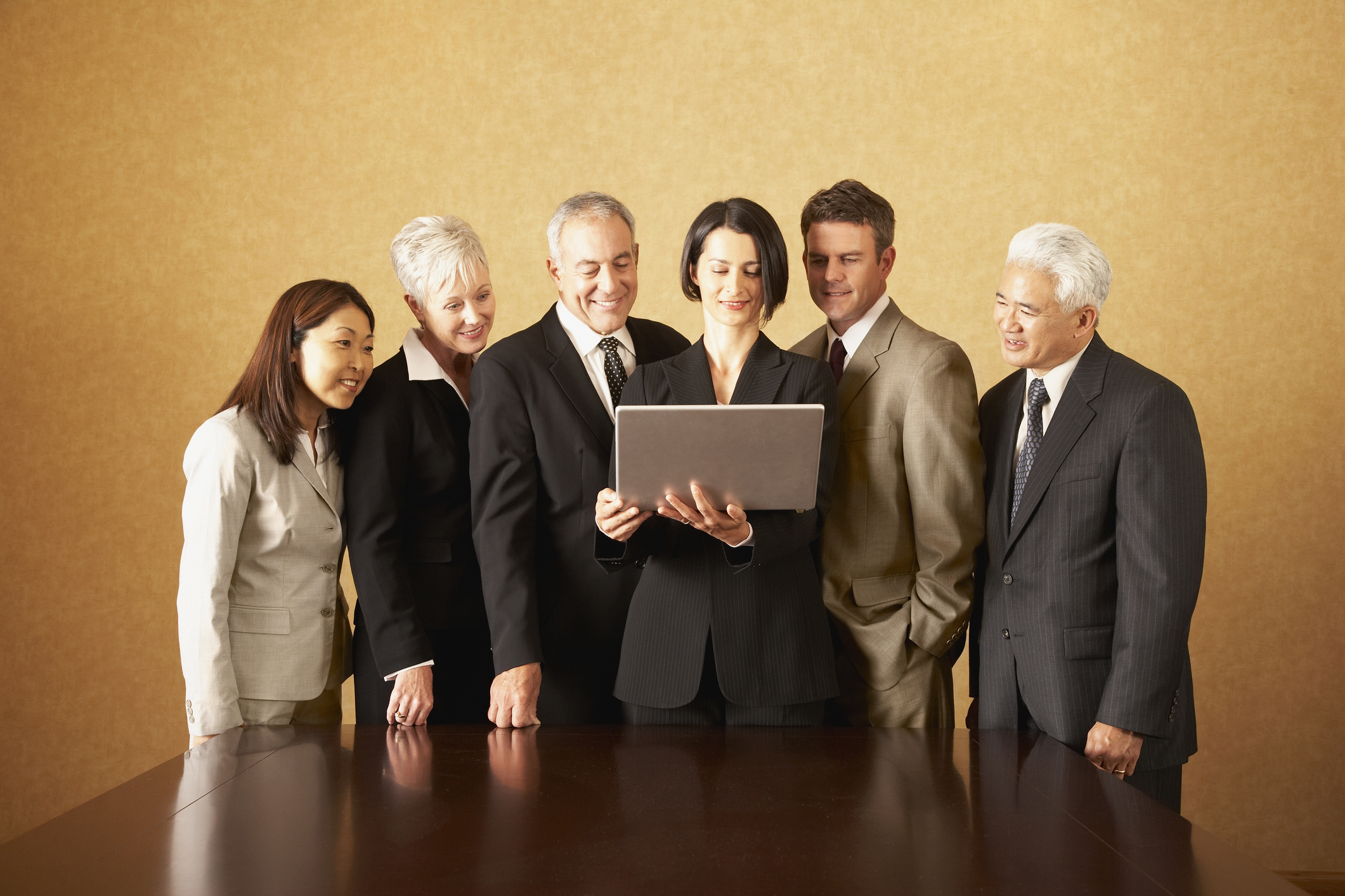 Group of businesspeople standing with laptop behind table