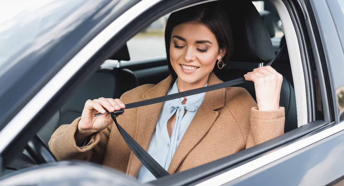 stylish woman in autumn outfit putting on safety belt while sitting in car on blurred foreground