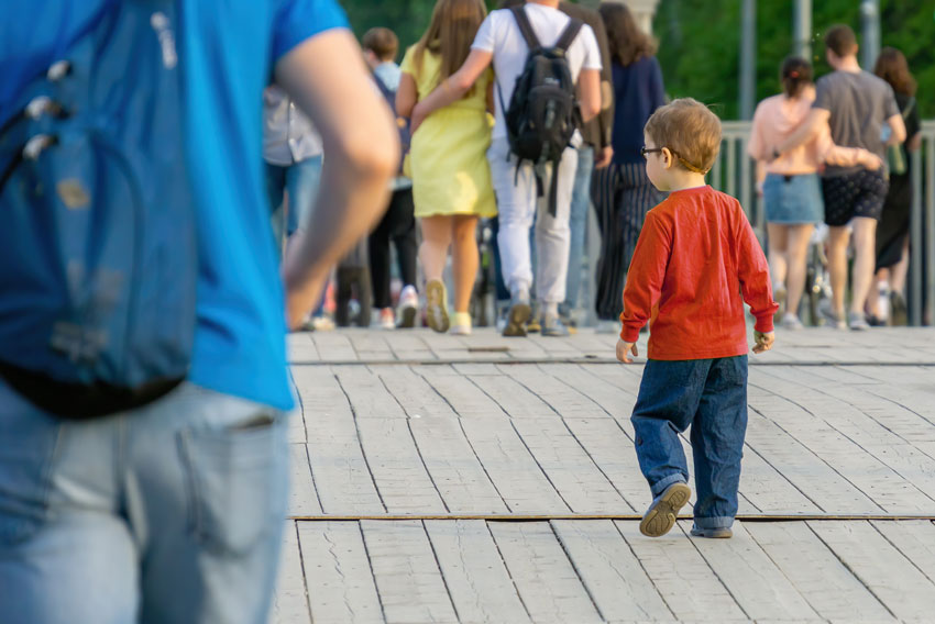Izgubljen otrok v množici - deček v rdeči majici sam hodi med množico odraslih