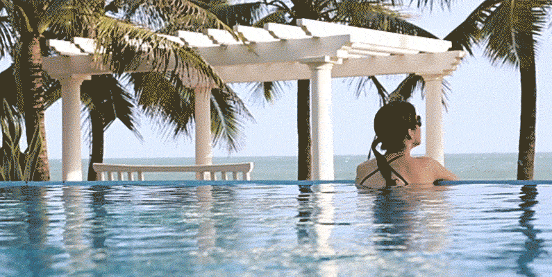 Travel cinemagraph of a woman relaxing inside an infinity pool at a tropical resort.