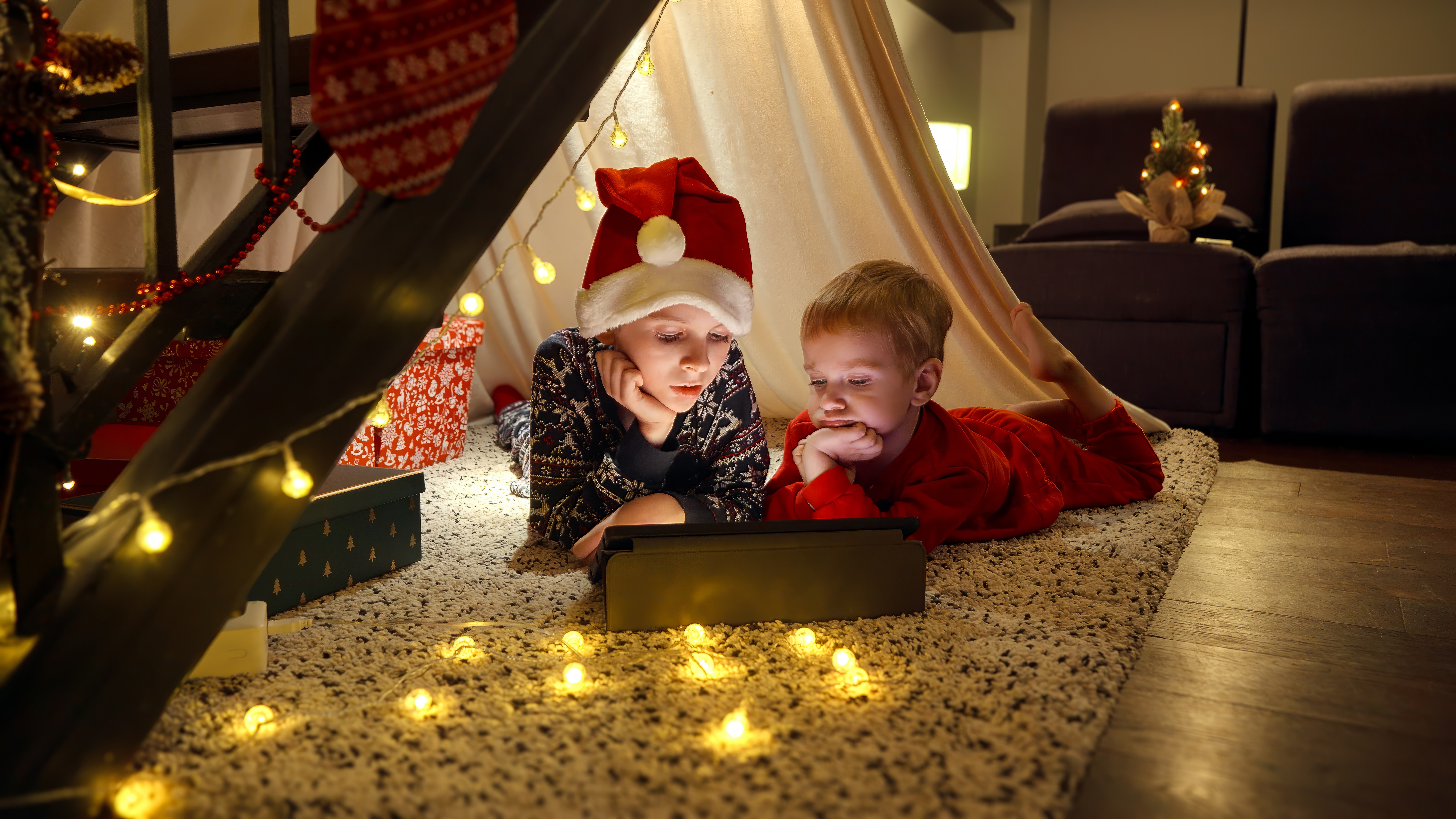 Children in festive hats under indoor den enjoying tablet time