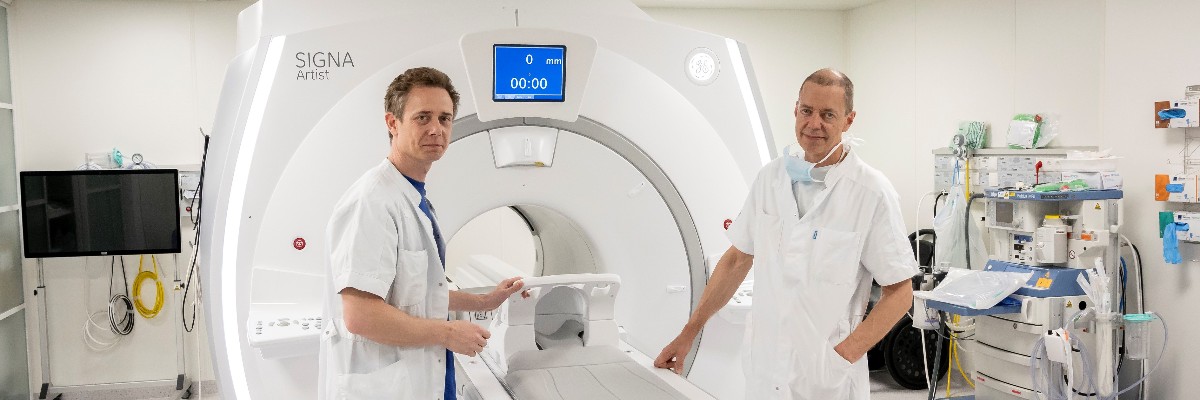 Neurokirurgerne Rune Rasmussen og Bo Jespersen foran deres MR-scanner, SIGNA™ Artist fra GE Healthcare, og det særlige Surgical Suite transportleje, som gør det muligt at flytte en patient frem og tilbage mellem operationsstue og scanner under en hjerneoperation – uden at patientens hoved rykkes ud af position.