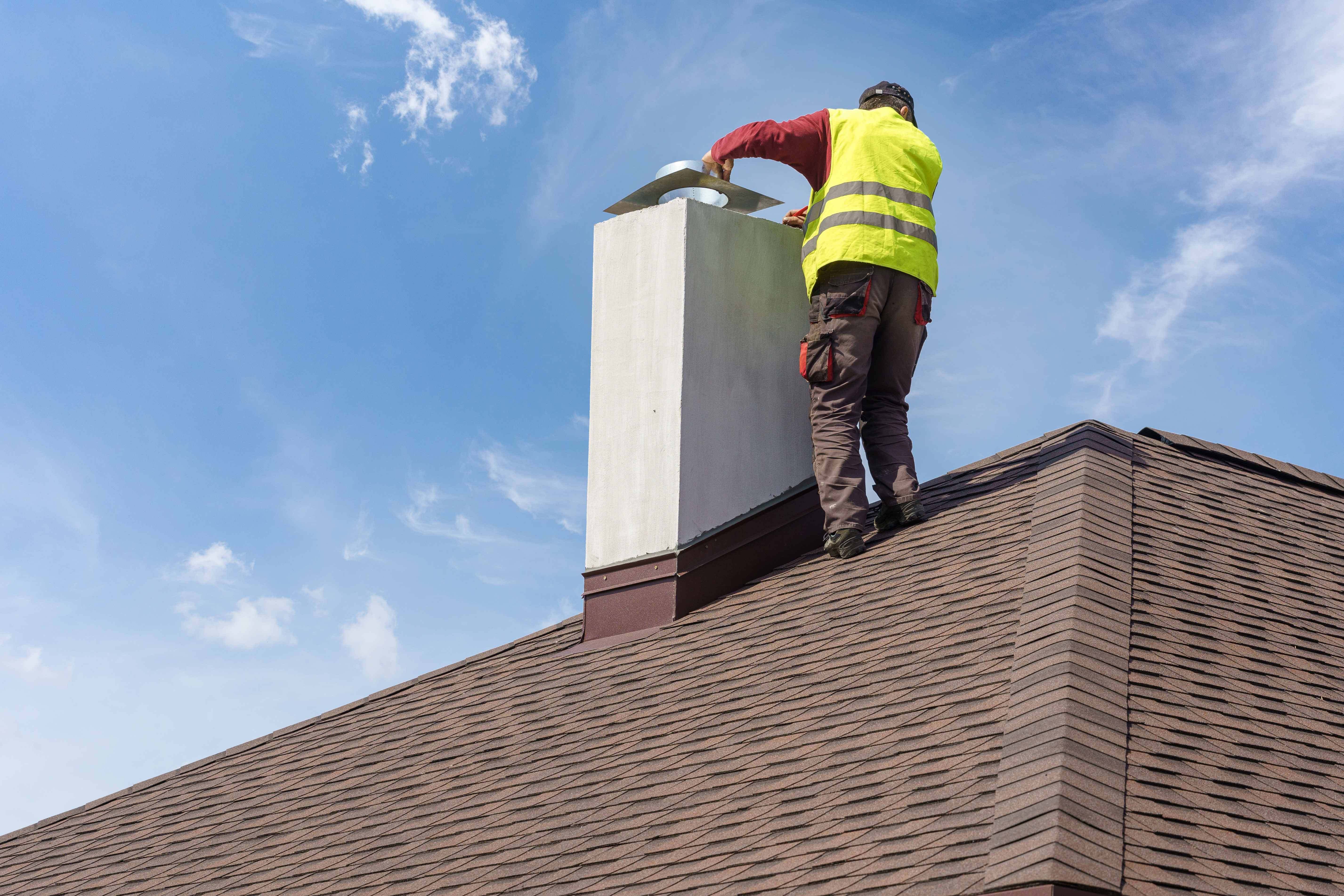 Skilled workman in protective work wear and special uniform install chimney on roof top of new house under construction