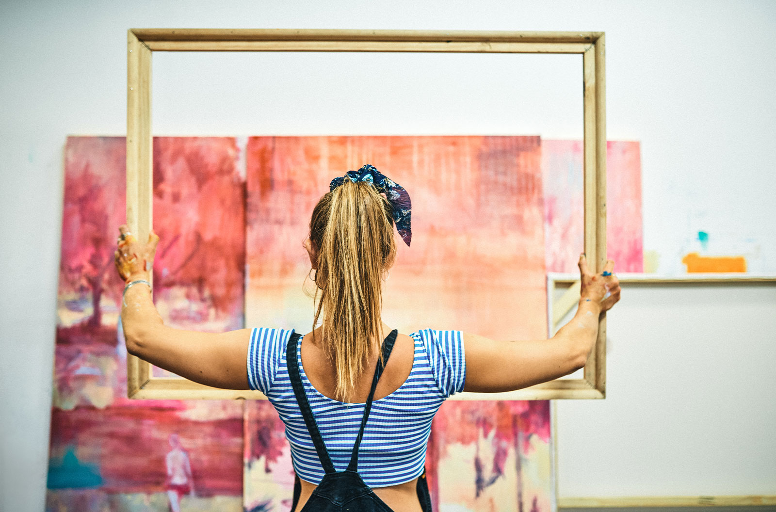 Rearview shot of a blonde woman standing alone and holding a wooden frame in her art studio