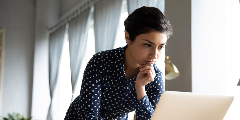 A woman in a well lit room thinking pensively in a polkadot blouse