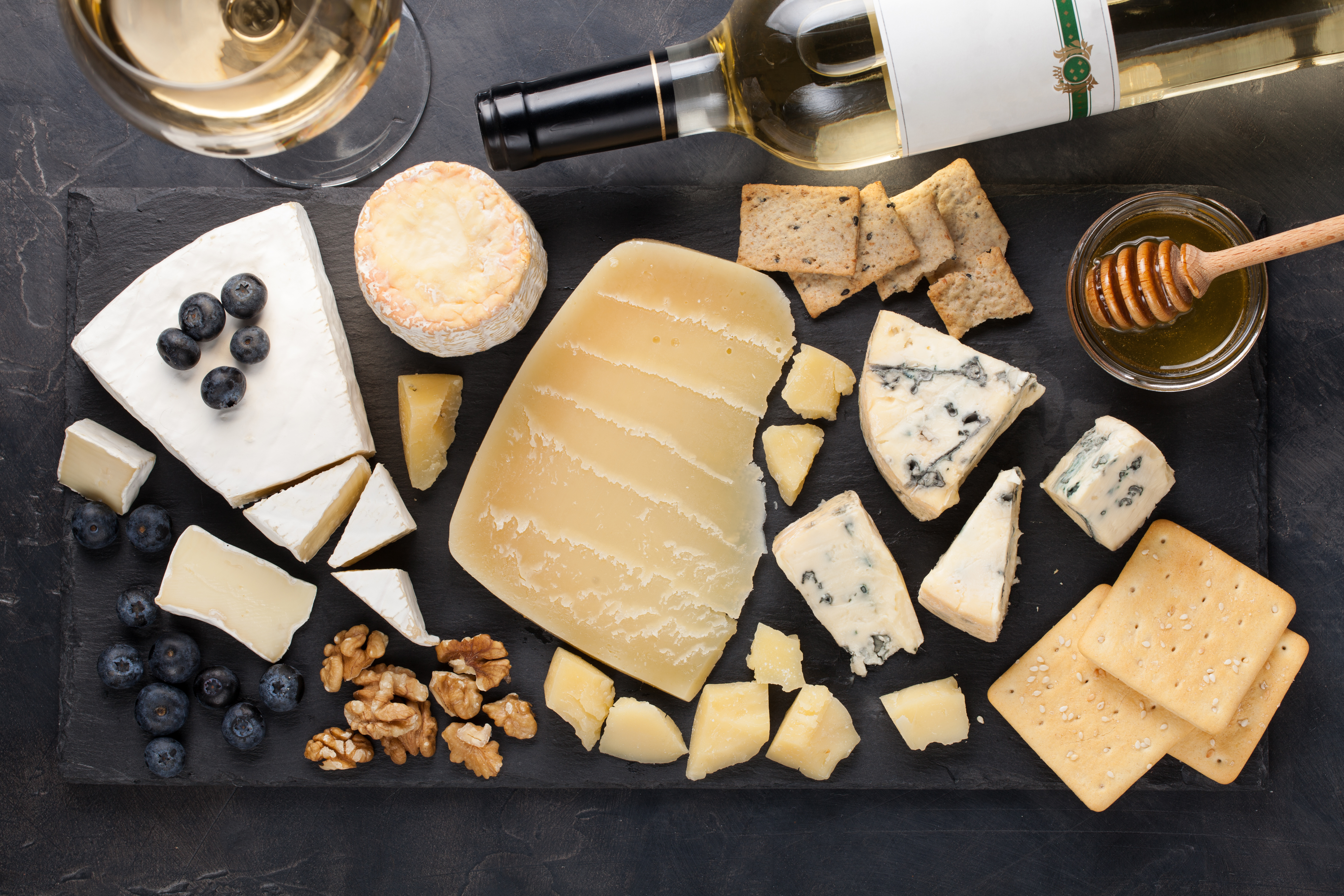 Tasting cheese dish on a dark stone plate. Food for wine and romantic date, cheese delicatessen on a black concrete background. Top view