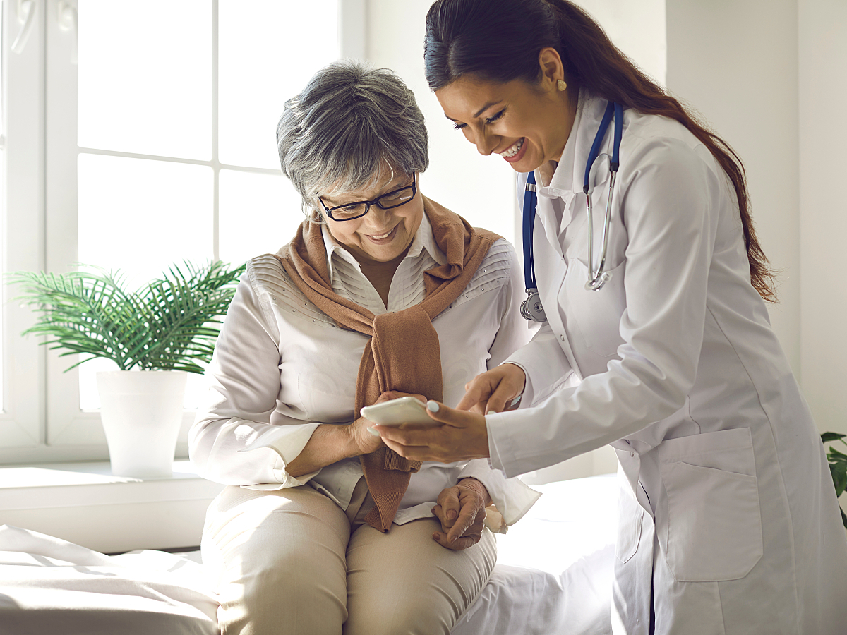A home health aide helps an elderly patient with her wearable device. 