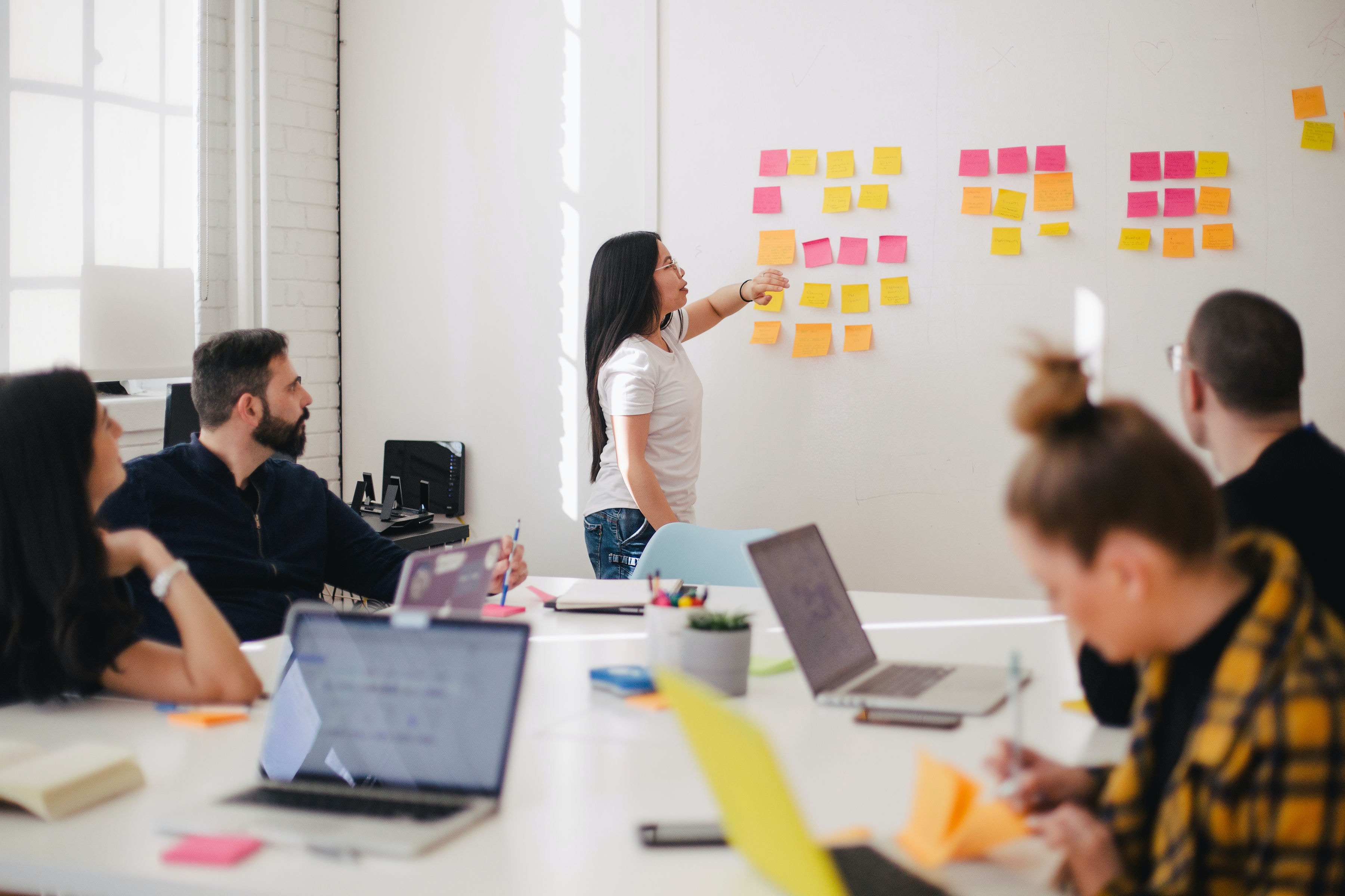 Woman placing post-it notes on wall in front of seated team in meeting