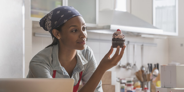 Mixed race baker admiring cupcake in commercial kitchen