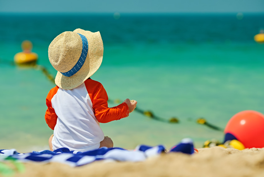 Otrok na plaži, starši upoštevajo navodila za izpostavljanje soncu oziroma sončenje
