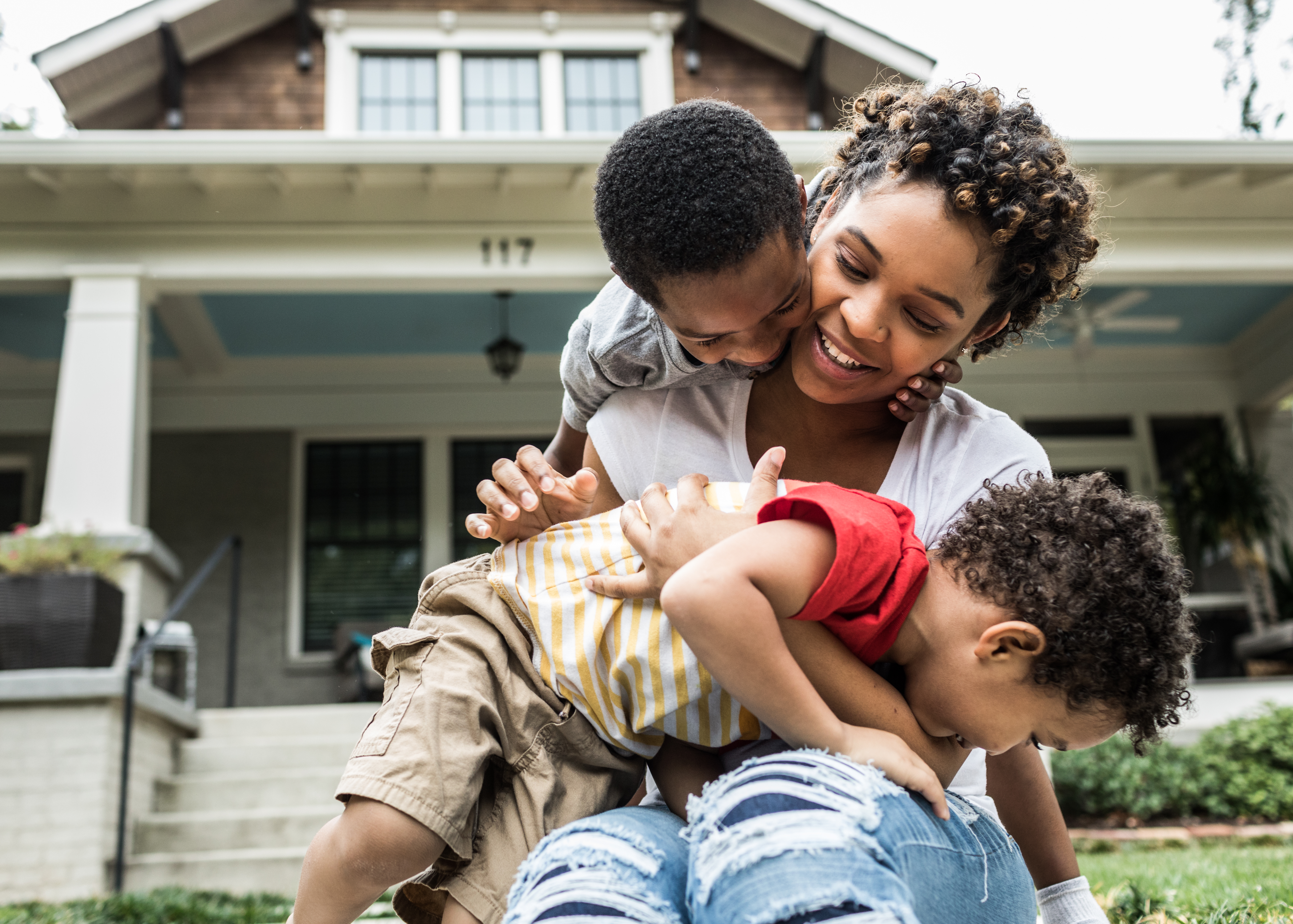 Single mother playing with young sons in front of house