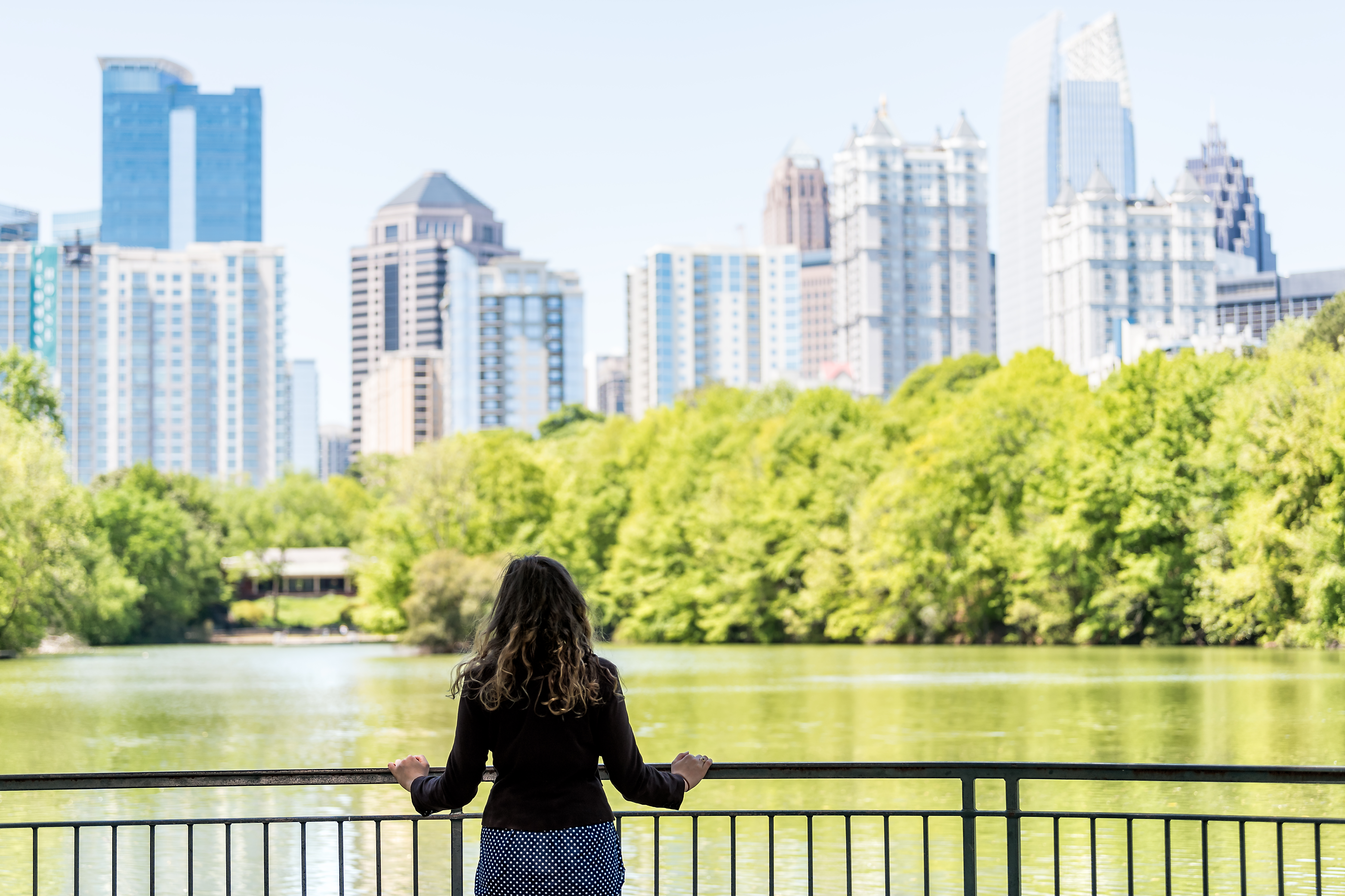 Young woman standing in Piedmont Park in Atlanta, Georgia looking at scenic water, and cityscape skyline of urban city skyscrapers downtown, Lake Clara Meer