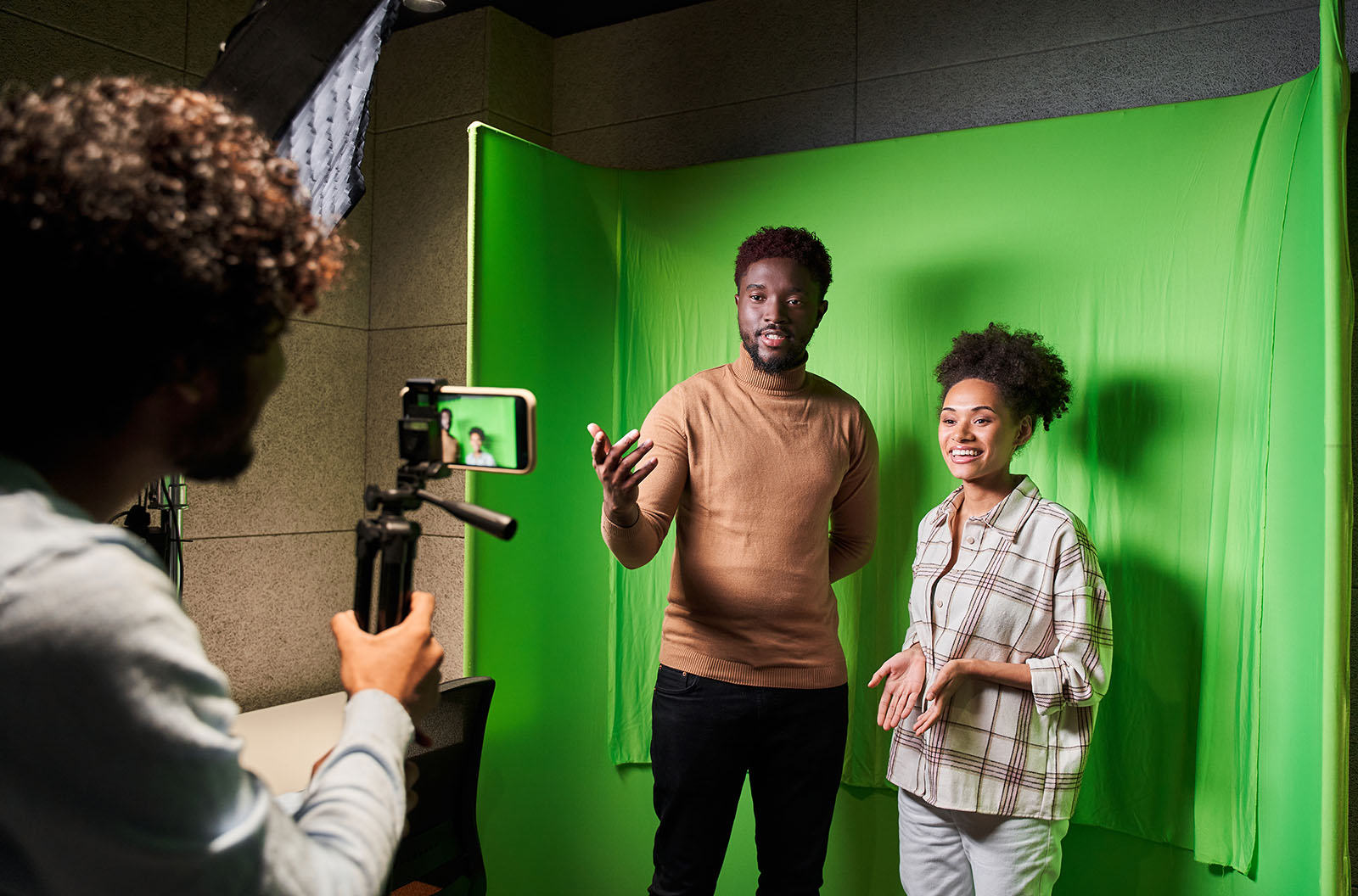 Two people being filmed on an iPhone in front of a green screen. 