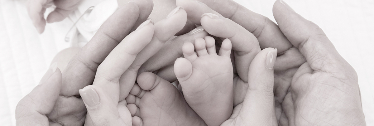 Black and white image of parents' hands encircling their newborn's feet.