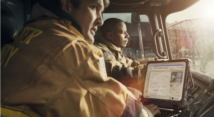 two firefighters use a durable laptop while sitting in a vehicle.