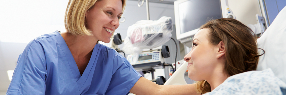 A female patient in a hospital bed speaks with a nurse. 