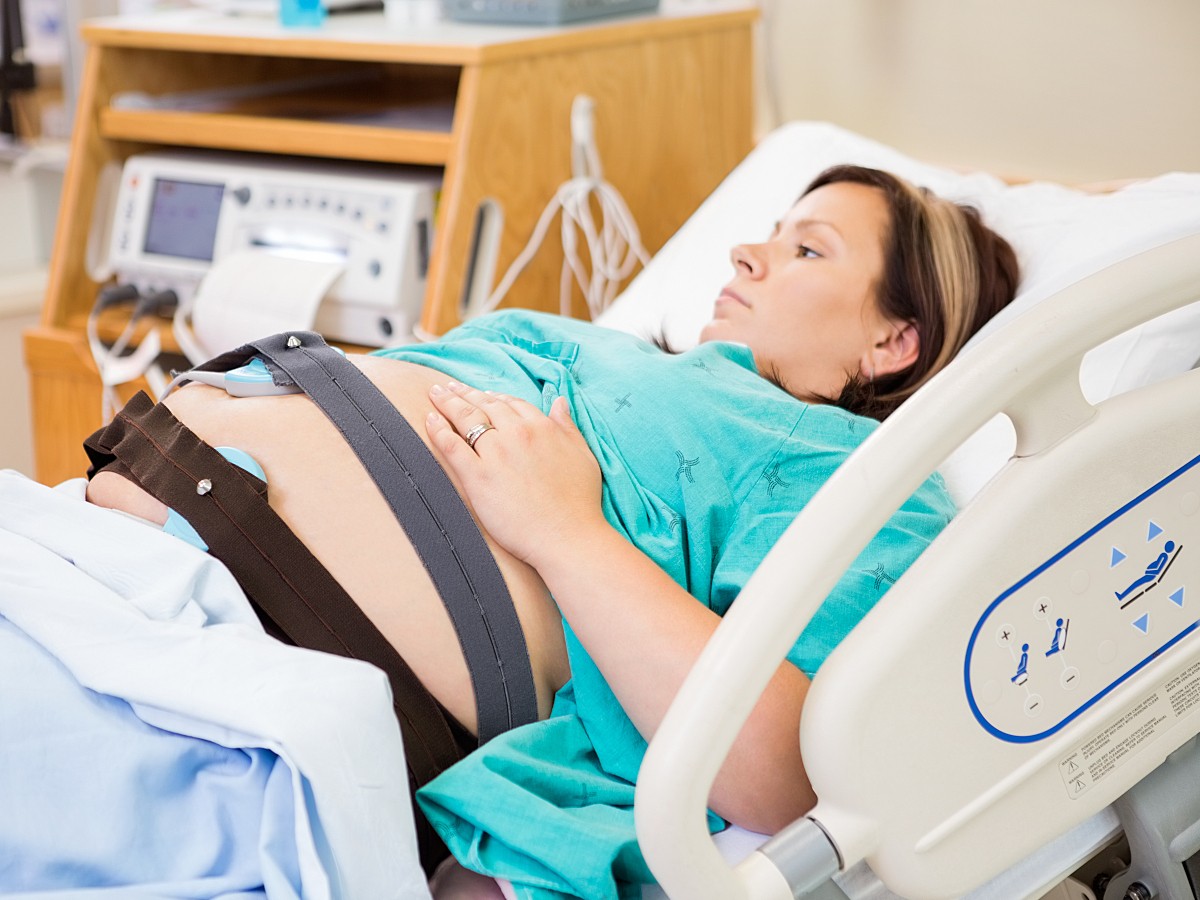 <p>A pregnant woman with electrodes on her stomach lying in hospital bed.</p>