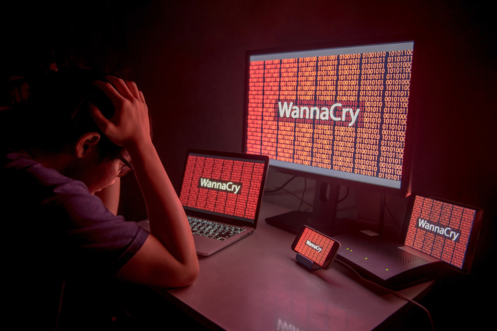 Young Asian male frustrated, confused and headache by WannaCry ransomware attack on desktop screen, notebook and smartphone, cyber attack internet security concept