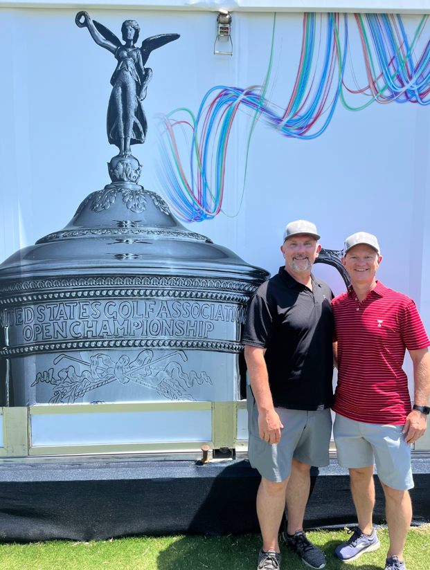 Two men standing in front of a large picture of a statueDescription automatically generated with low confidence
