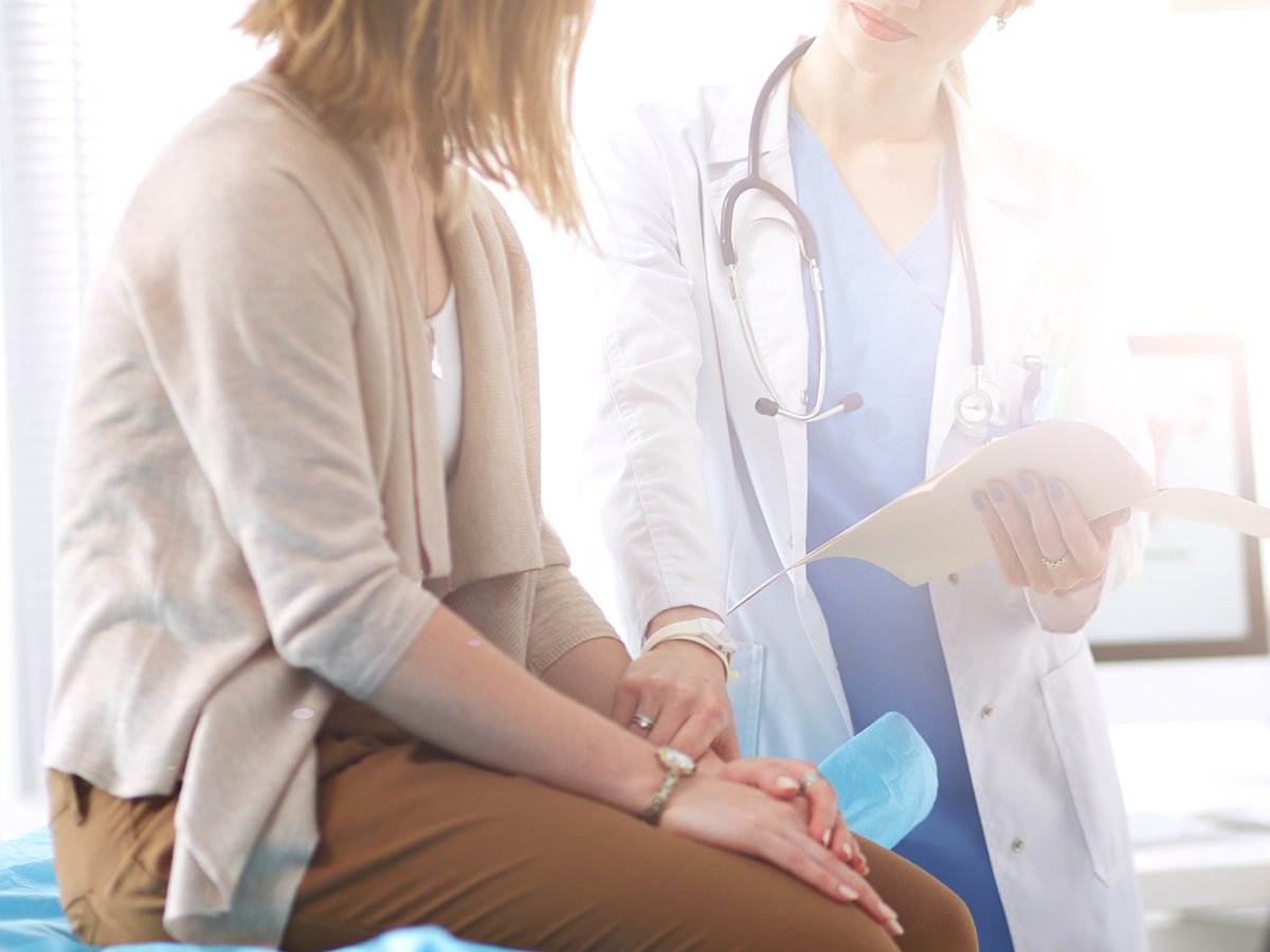 A physician speaks with a patient seated on an exam table to discuss the patient's care plan
