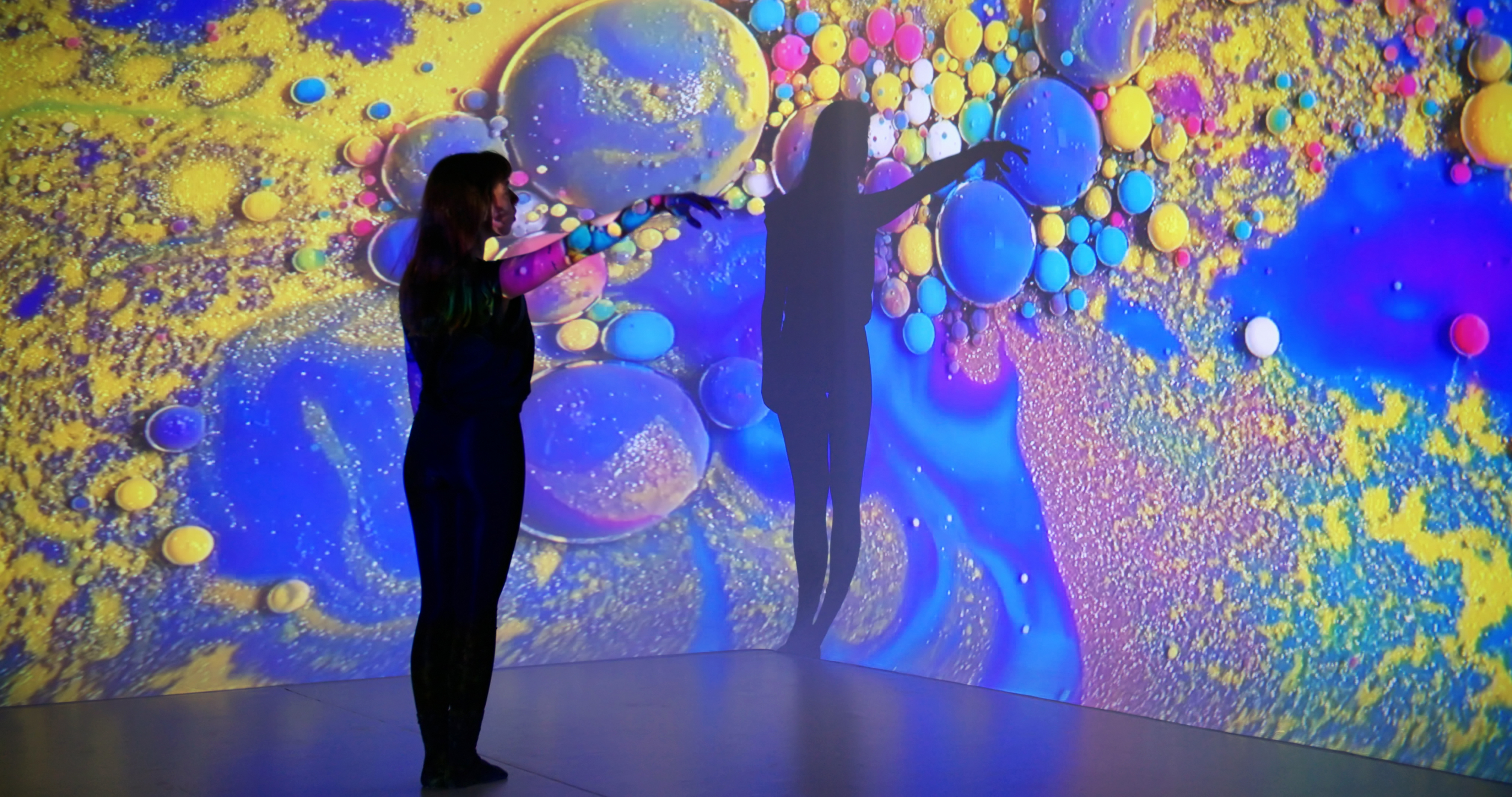 A woman enjoys an immersive experience using projection mapping to cover a wall in abstract art.