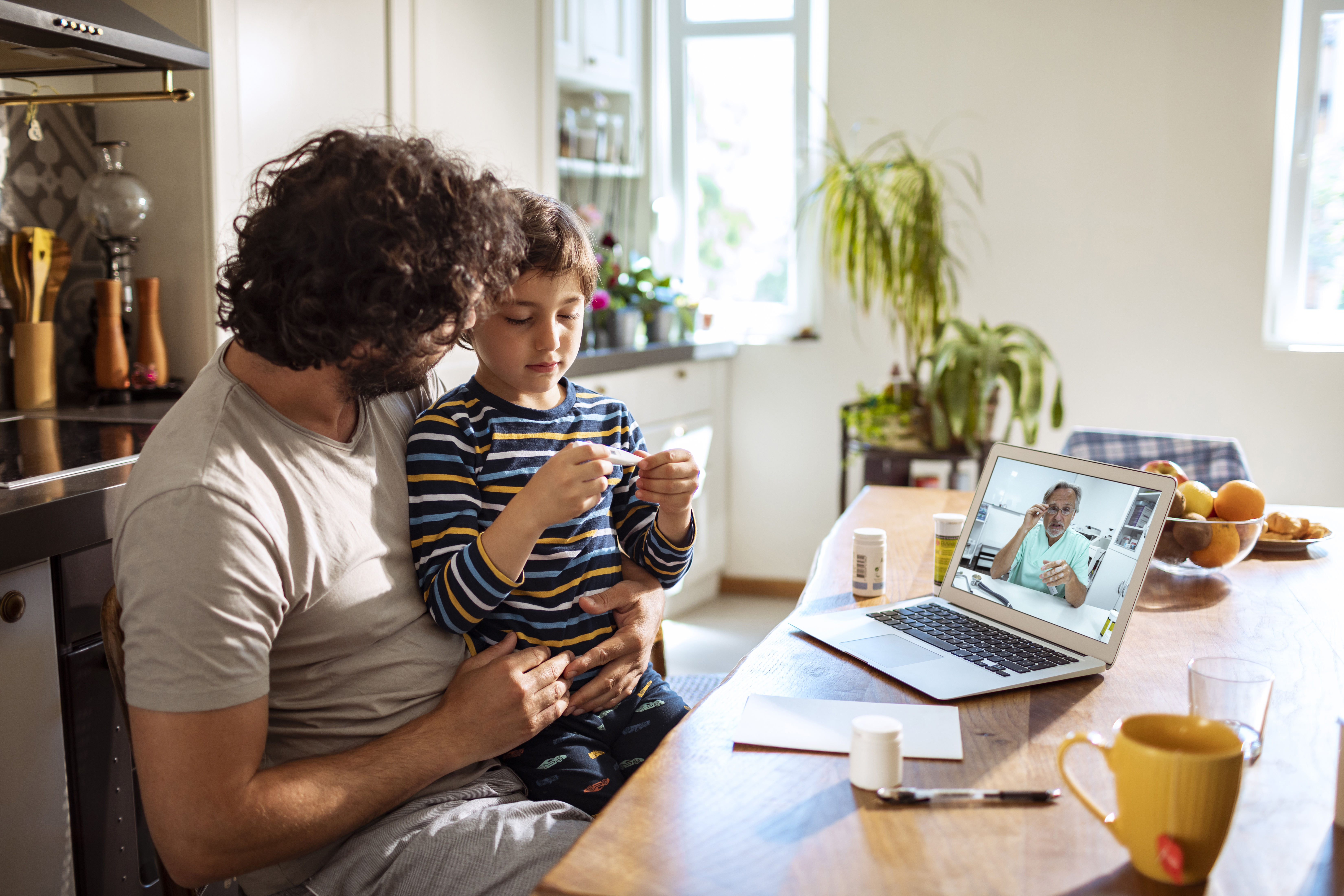 Close up of a father with his son in the lap consulting with the doctor over a laptop