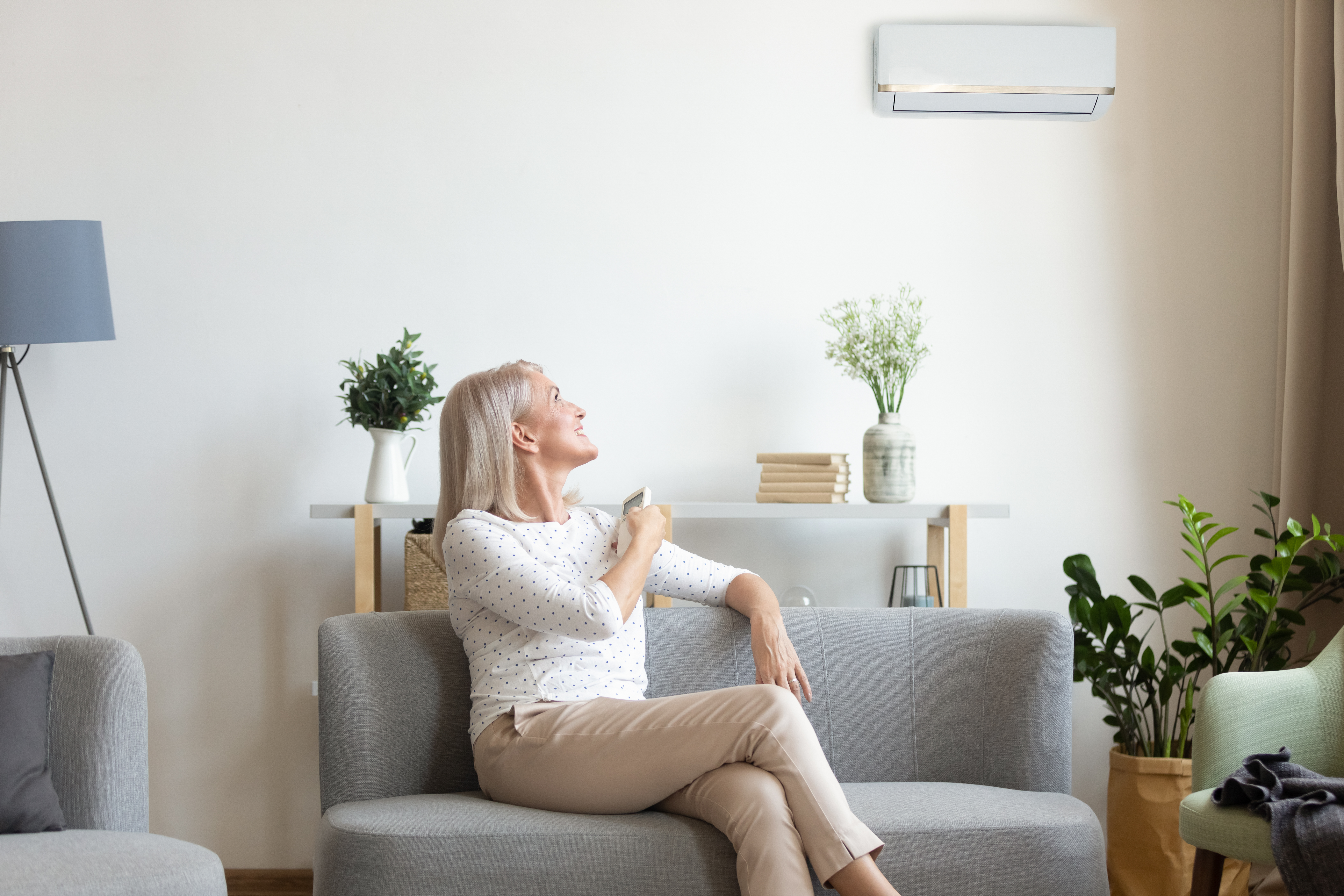 Middle aged woman switching on air conditioner in living room