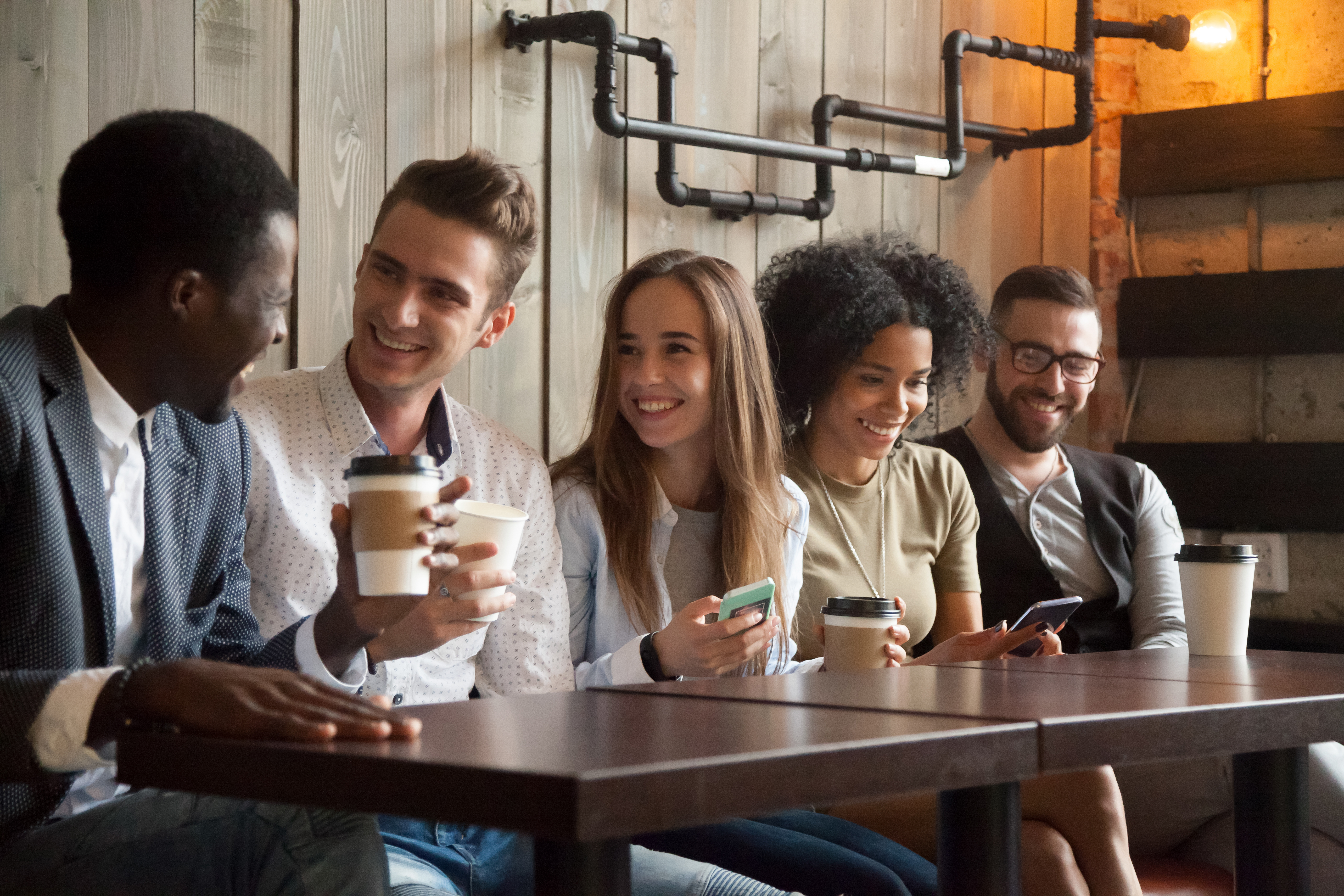 Happy multi-ethnic group of friends talking using smartphones at meeting