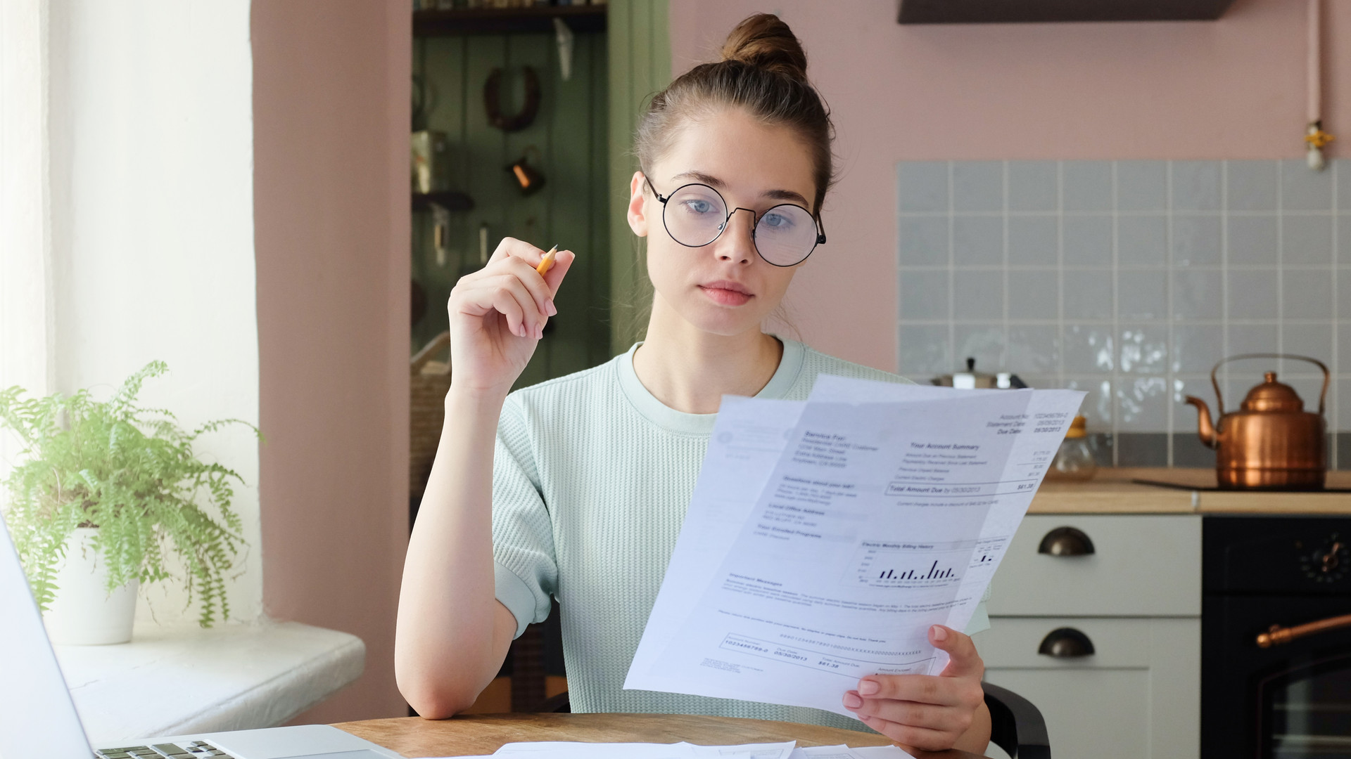 Portrait of young woman, sitting at kitchen table, filling application form, calculating expences, trying to solve budget problems, looking at papers, managing with utility bills